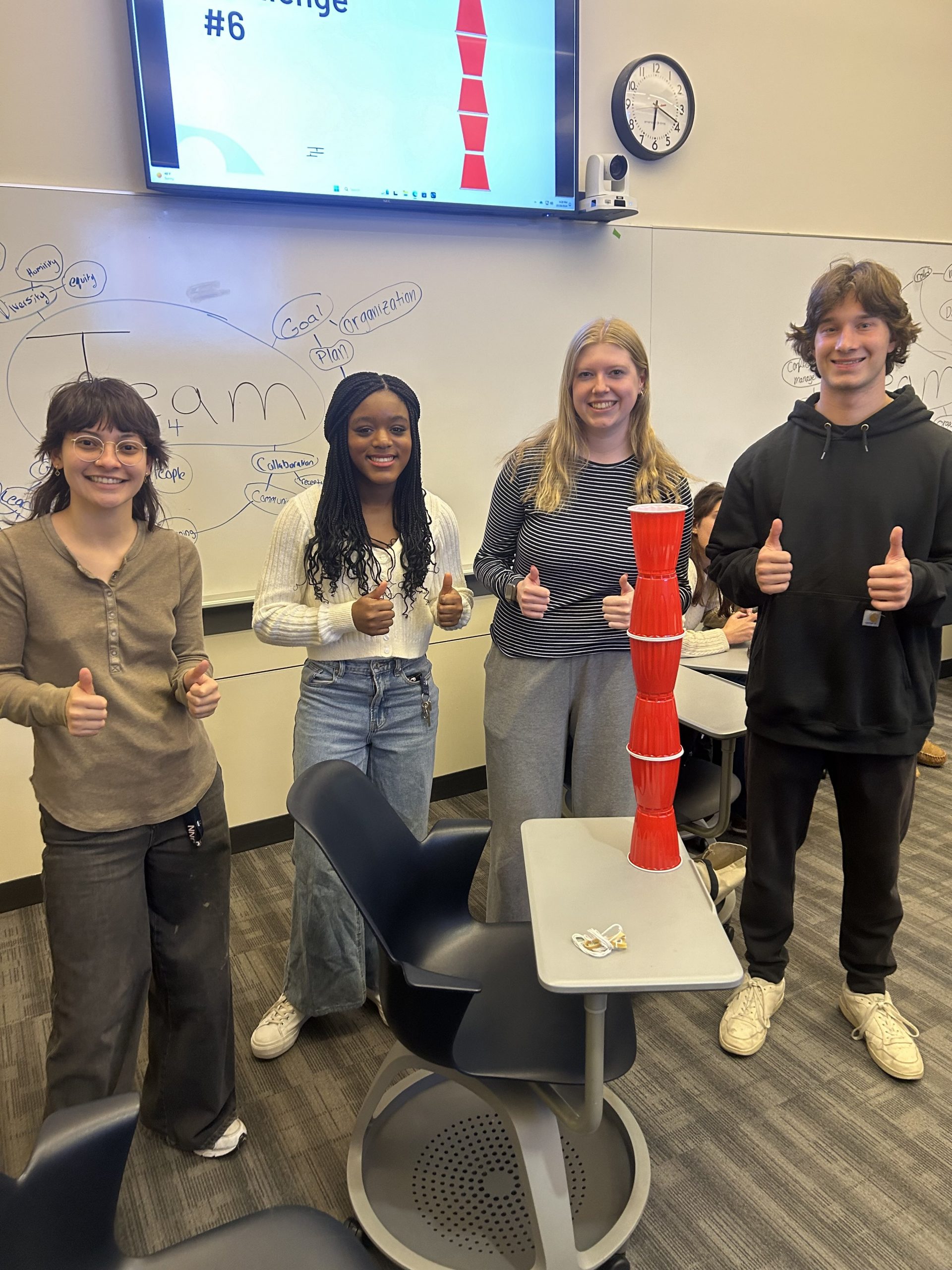 Students pose with a tower of red plastic cups they have stacked for an activity